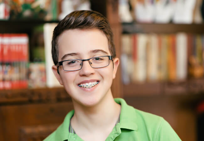 Teenage boy in a green shirt smiles while wearing braces and glasses in a library in Lytle, TX