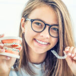 Brunette teenager holds up braces vs Invisalign aligners to compare which is right for her