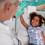 Little girl at the dentist smiles while high-fiving her dentist before receiving dental sedation