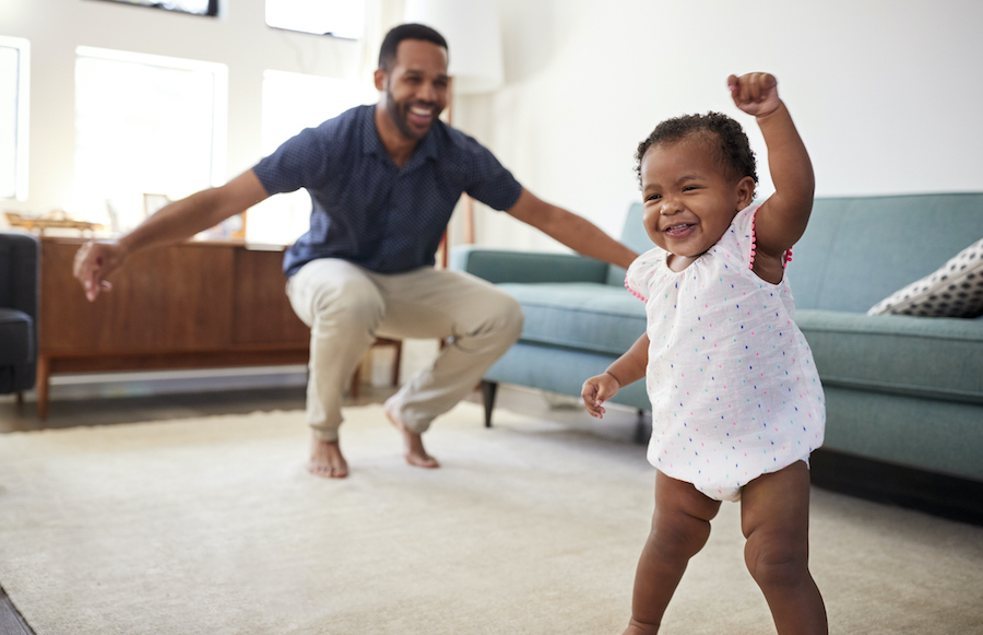Black teething toddler dances in the family room with her dad